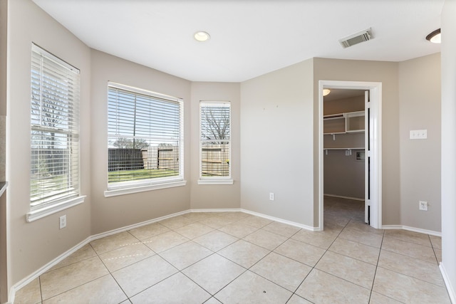 unfurnished bedroom with light tile patterned flooring, visible vents, a walk in closet, and baseboards