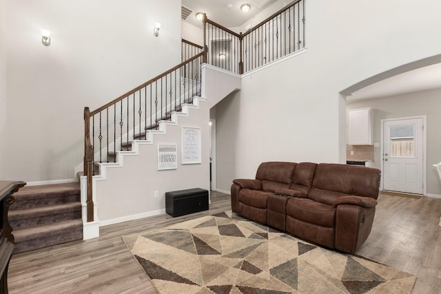 living area featuring visible vents, baseboards, stairway, a high ceiling, and light wood-style floors