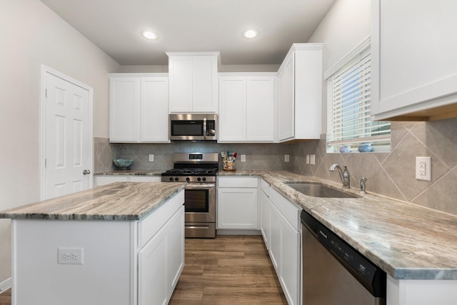 kitchen with wood finished floors, a sink, stainless steel appliances, white cabinets, and a center island