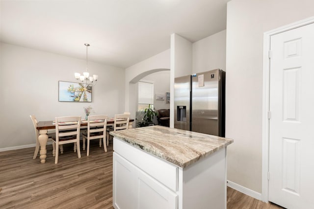 kitchen featuring light stone countertops, light wood-style flooring, stainless steel fridge with ice dispenser, arched walkways, and white cabinetry