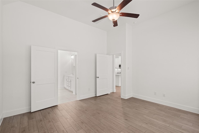 unfurnished bedroom with light wood-style flooring, baseboards, ensuite bathroom, and high vaulted ceiling