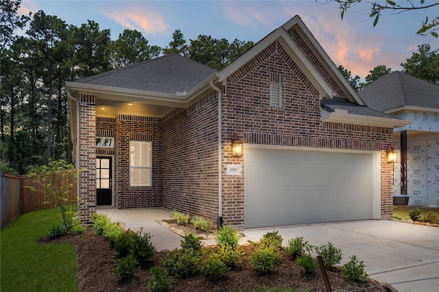 view of front facade featuring driveway, fence, roof with shingles, a garage, and brick siding