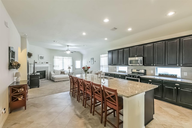 kitchen featuring visible vents, a center island with sink, a sink, dark cabinetry, and stainless steel appliances