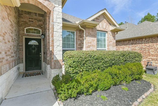 doorway to property featuring brick siding, stone siding, and roof with shingles