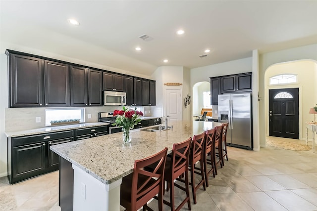 kitchen featuring visible vents, a sink, arched walkways, stainless steel appliances, and a kitchen island with sink