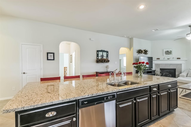 kitchen featuring arched walkways, a sink, open floor plan, stainless steel dishwasher, and dark cabinets