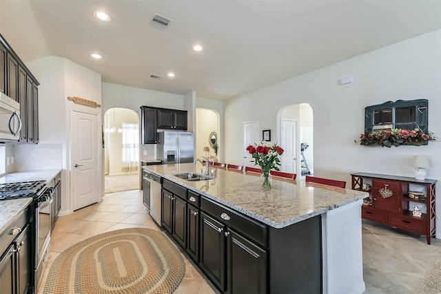 kitchen featuring visible vents, a center island with sink, a sink, arched walkways, and appliances with stainless steel finishes