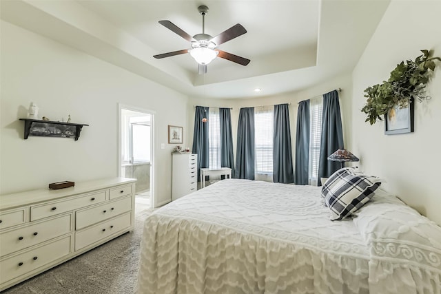 bedroom with ceiling fan, ensuite bath, a tray ceiling, and carpet floors