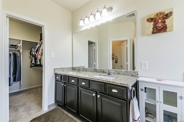 full bathroom with double vanity, visible vents, a walk in closet, and a sink