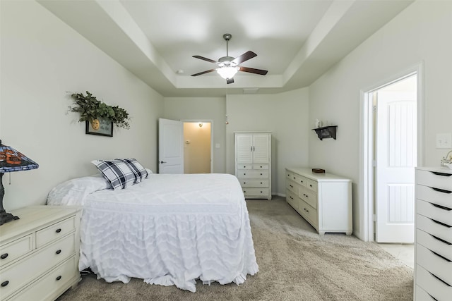 bedroom with light colored carpet, a ceiling fan, and a tray ceiling