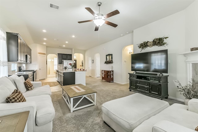 living area with a ceiling fan, visible vents, arched walkways, and light colored carpet