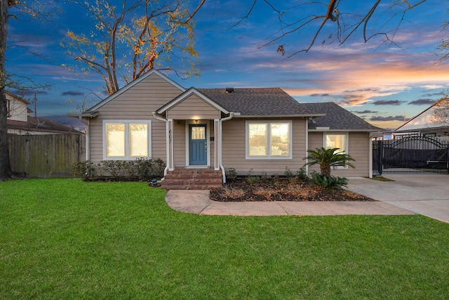 view of front of house featuring a lawn, fence, roof with shingles, and a gate