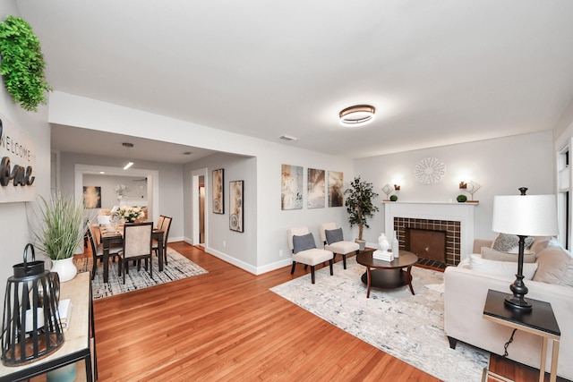 living room with a tiled fireplace, light wood-style floors, visible vents, and baseboards