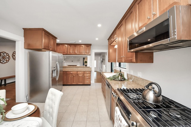 kitchen with light tile patterned floors, recessed lighting, a sink, appliances with stainless steel finishes, and brown cabinets