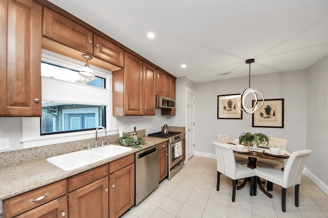 kitchen featuring hanging light fixtures, brown cabinetry, appliances with stainless steel finishes, and a sink