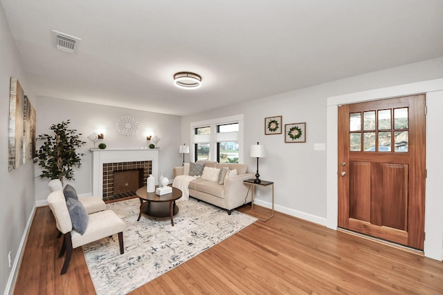 living area with visible vents, baseboards, a tiled fireplace, and light wood finished floors