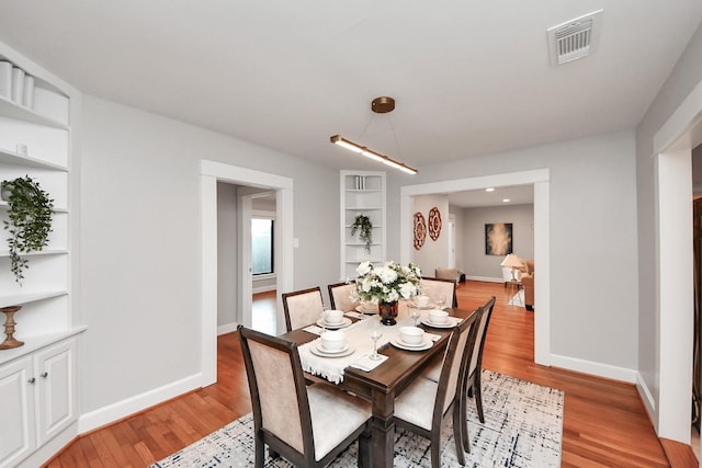 dining room featuring light wood-type flooring, visible vents, built in shelves, and baseboards