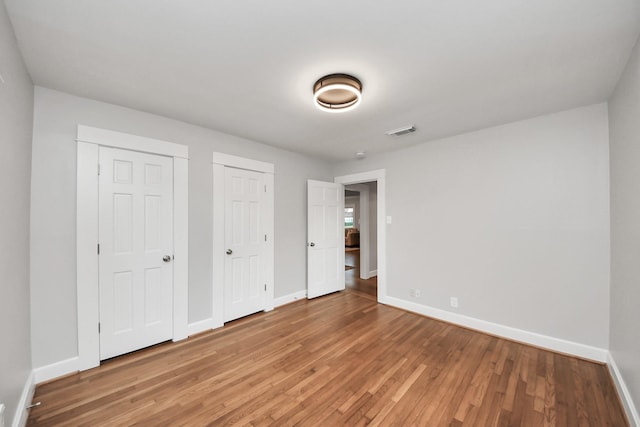 unfurnished bedroom featuring light wood finished floors, visible vents, baseboards, and multiple closets