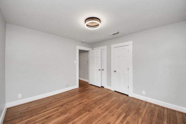 unfurnished bedroom featuring wood finished floors, visible vents, two closets, and baseboards