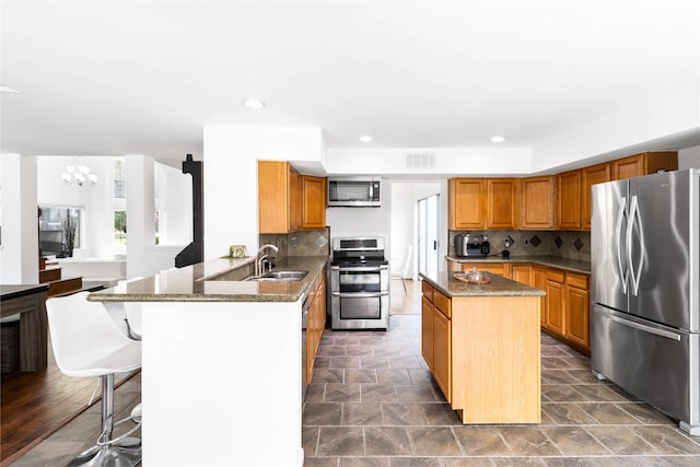 kitchen featuring backsplash, a kitchen island, appliances with stainless steel finishes, a peninsula, and a sink