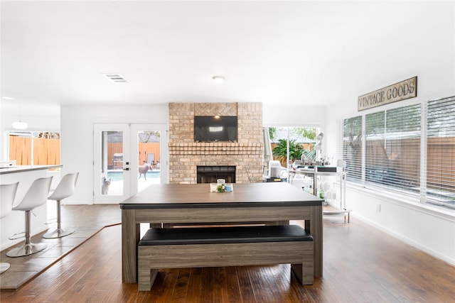 dining area with hardwood / wood-style floors, a brick fireplace, french doors, and visible vents