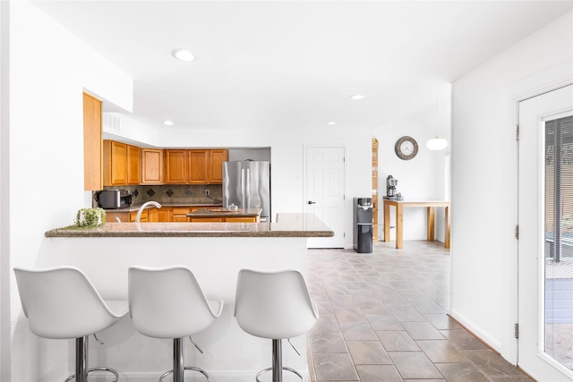 kitchen with decorative backsplash, recessed lighting, a peninsula, a kitchen breakfast bar, and freestanding refrigerator