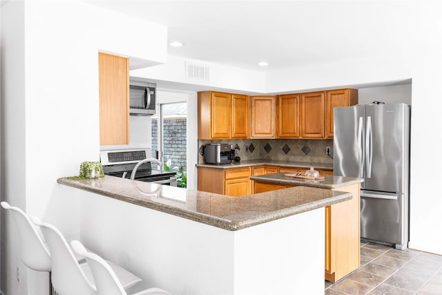 kitchen featuring visible vents, light stone counters, tasteful backsplash, stainless steel appliances, and a peninsula