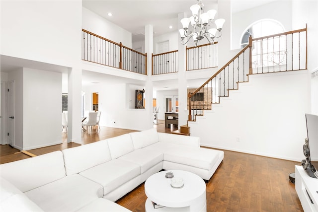 living room featuring baseboards, a chandelier, stairs, a towering ceiling, and wood-type flooring