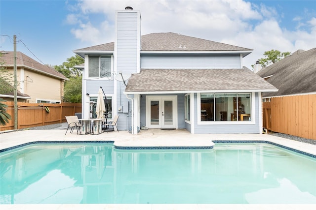 back of property featuring french doors, roof with shingles, a fenced backyard, and a chimney