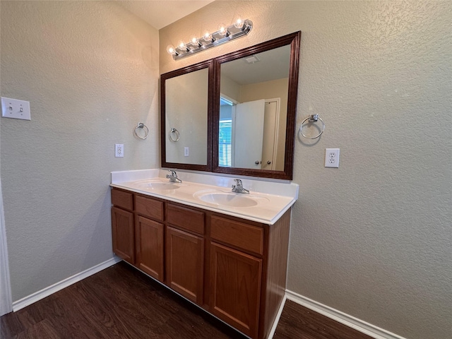 full bathroom featuring double vanity, wood finished floors, a textured wall, and a sink