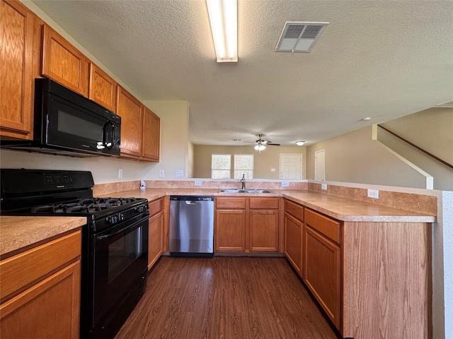 kitchen with visible vents, black appliances, a sink, dark wood-style floors, and a peninsula