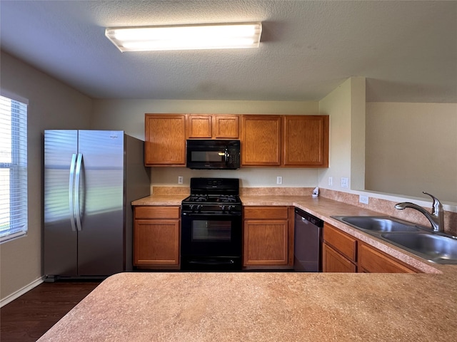 kitchen with brown cabinets, dark wood-type flooring, black appliances, a sink, and light countertops