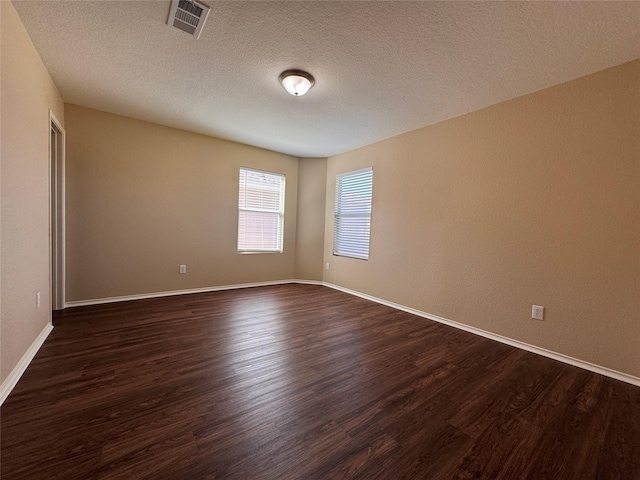 unfurnished room featuring visible vents, baseboards, a textured ceiling, and dark wood-style floors