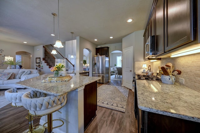 kitchen featuring stainless steel appliances, arched walkways, tasteful backsplash, and open floor plan