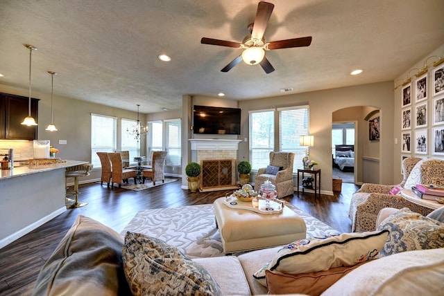 living room featuring arched walkways, dark wood finished floors, a fireplace, and a wealth of natural light