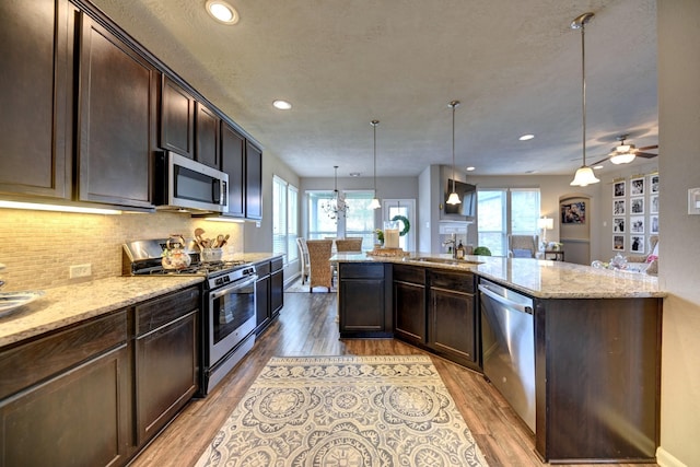 kitchen with light stone countertops, dark brown cabinetry, light wood-style floors, appliances with stainless steel finishes, and tasteful backsplash