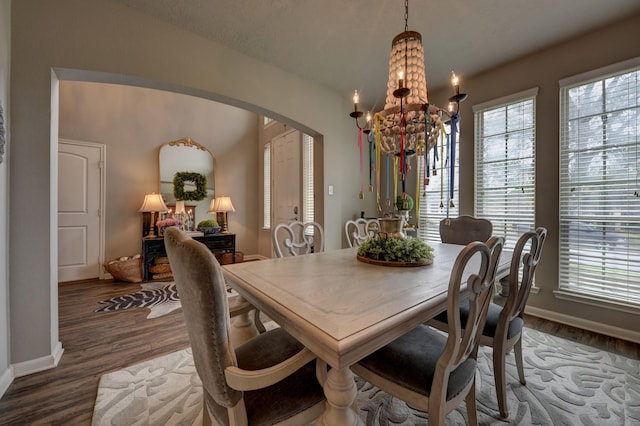 dining room with baseboards, wood finished floors, arched walkways, and a chandelier