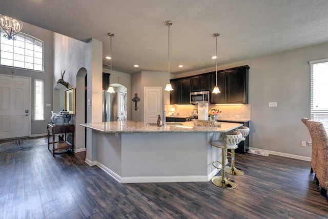 kitchen with a sink, tasteful backsplash, dark wood finished floors, stainless steel appliances, and arched walkways