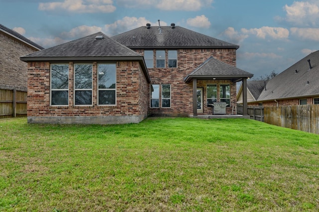 rear view of property with brick siding, a fenced backyard, a shingled roof, a patio area, and a lawn