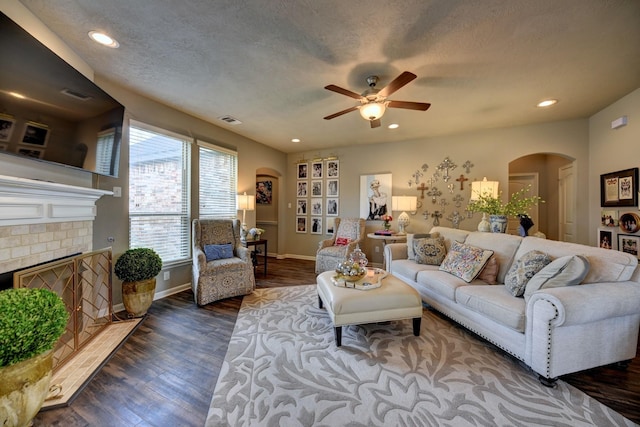 living area with wood finished floors, visible vents, a fireplace, arched walkways, and a textured ceiling