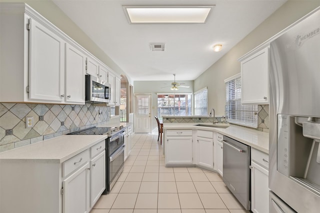 kitchen featuring light tile patterned floors, visible vents, a peninsula, a sink, and stainless steel appliances