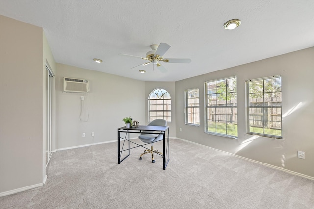 office space featuring a wall mounted air conditioner, a textured ceiling, carpet flooring, baseboards, and ceiling fan