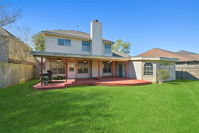 rear view of property featuring a lawn, a chimney, a deck, a fenced backyard, and a ceiling fan