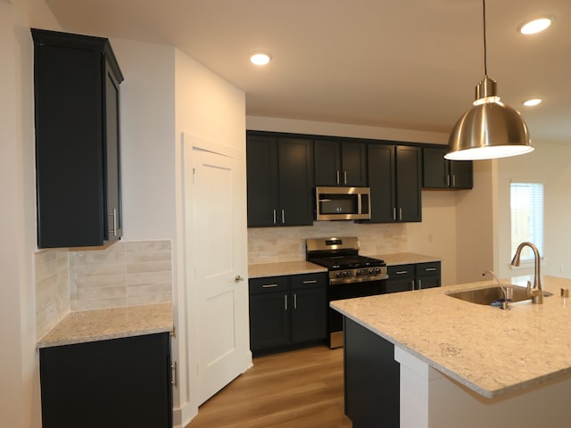 8035 Kay Harbor Dr, Cypress, TX 77433 - kitchen with appliances with stainless steel finishes, dark cabinetry, light wood-style flooring, light stone counters, and decorative backsplash