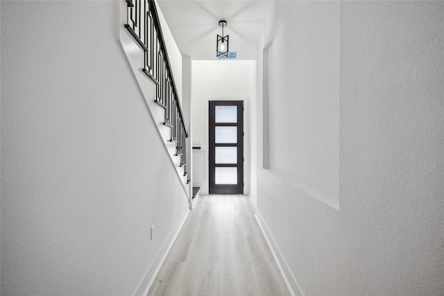 doorway featuring stairway, light wood-style flooring, baseboards, and a textured wall