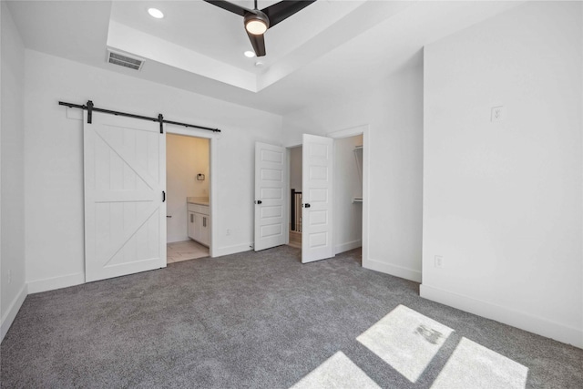 unfurnished bedroom featuring visible vents, a walk in closet, a tray ceiling, a barn door, and carpet