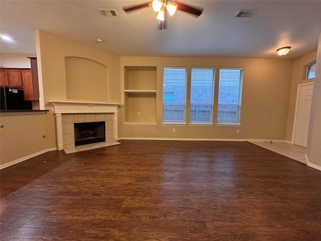 unfurnished living room with baseboards, visible vents, dark wood-style flooring, and a tile fireplace