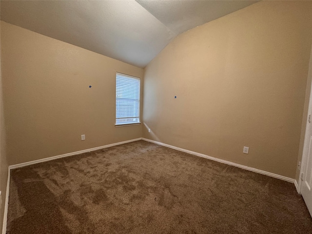 empty room featuring dark carpet, baseboards, and vaulted ceiling