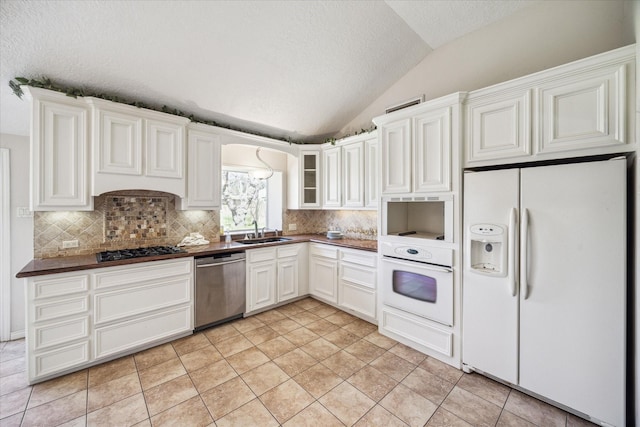 kitchen featuring a sink, dark countertops, white appliances, decorative backsplash, and lofted ceiling