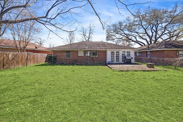 rear view of house featuring brick siding, french doors, a fenced backyard, a yard, and a patio